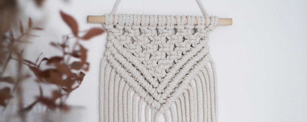 Macramé mural suspendu derrière un vase de fleurs séchées