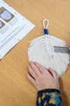 Mains d'une femme entrain de peigner une plume en macramé, à l'aide du tutoriel de la brochure d'apprentissage