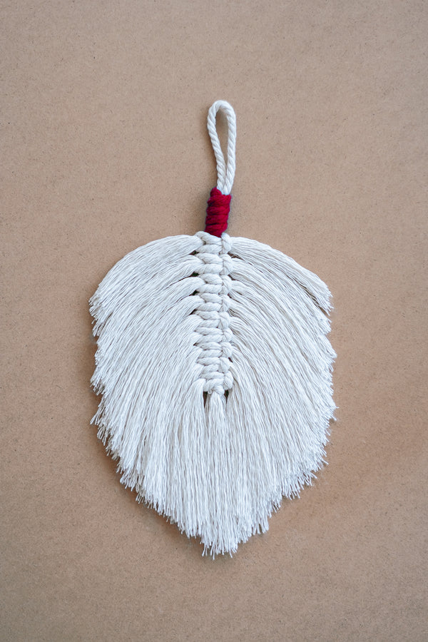 Plume en macramé beige et rouge sur une planche en liège