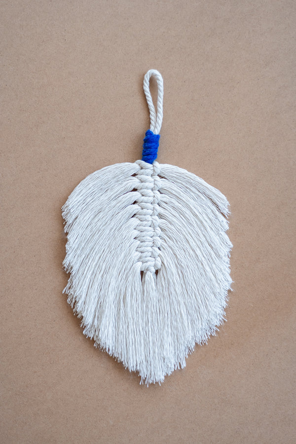 Plume en macramé beige et bleue sur une planche en liège