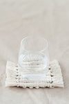 Première face d'un dessous de verre réversible en macramé avec un verre d'eau