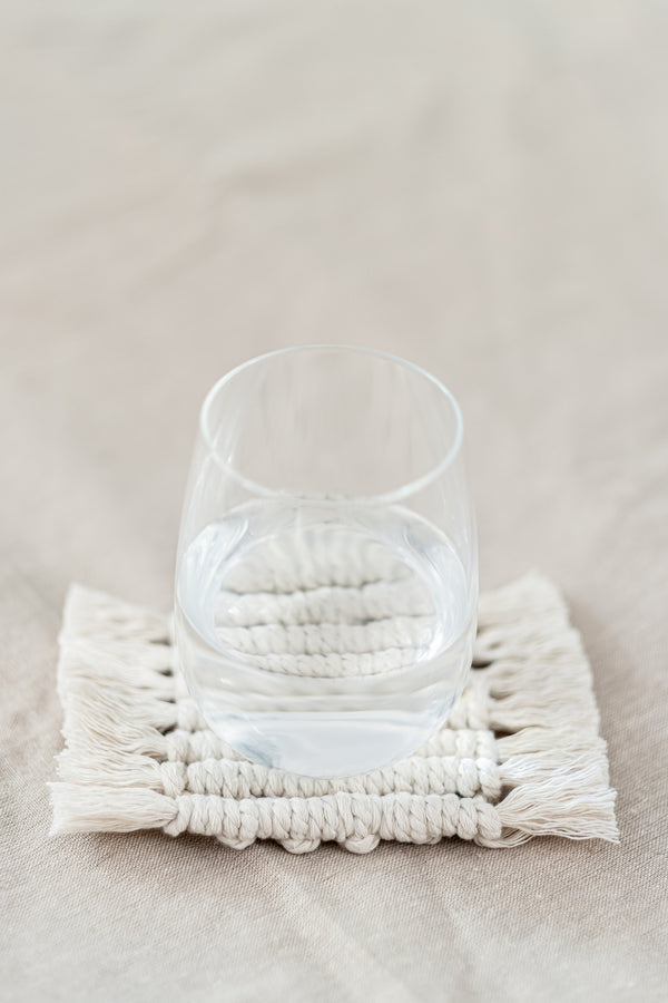 Première face d'un dessous de verre réversible en macramé avec un verre d'eau