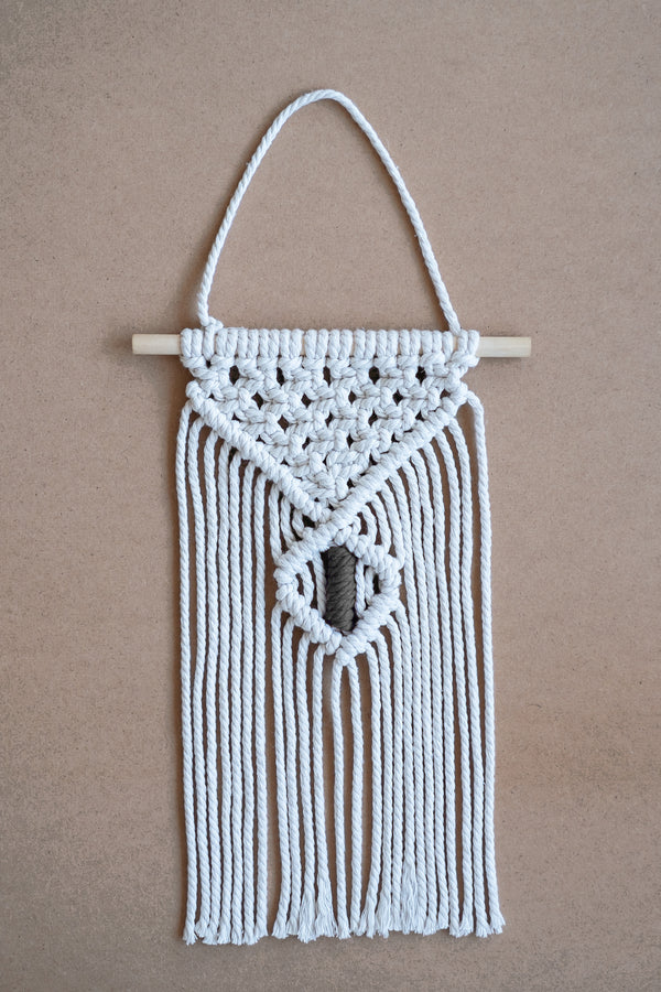 Macramé mural beige et gris sur une planche en liège