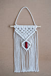 Macramé mural beige et rouge sur une planche en liège