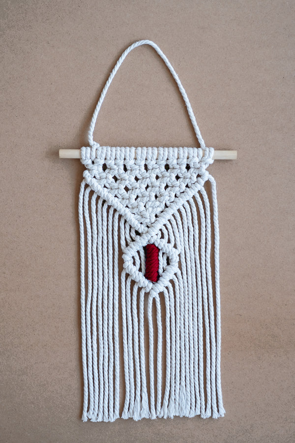 Macramé mural beige et rouge sur une planche en liège