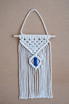 Macramé mural beige et bleu sur une planche en liège