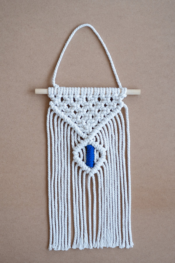Macramé mural beige et bleu sur une planche en liège