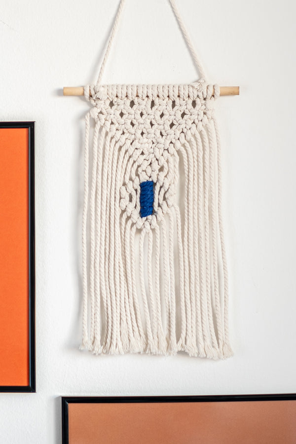 Petit macramé mural accroché au mur à côté de cadres décoratifs